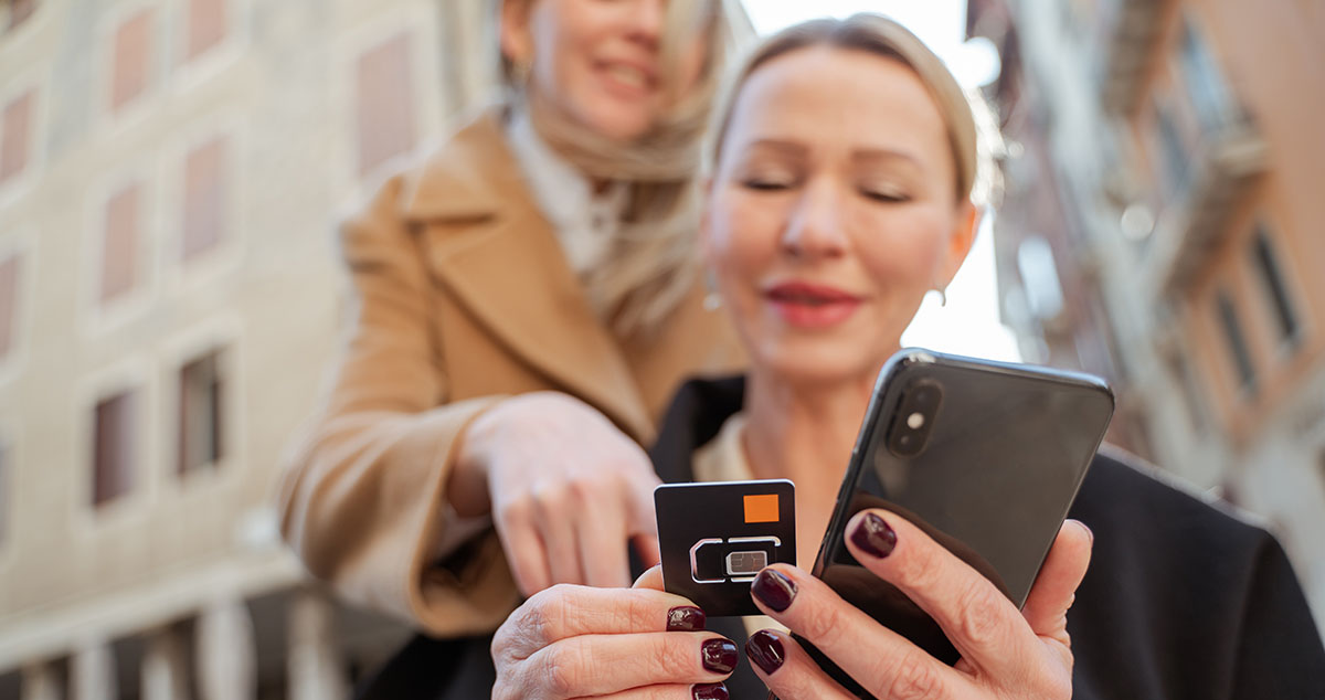 Blonde woman changing a sim card in her ohone, her freind helping digital nomads eSIM